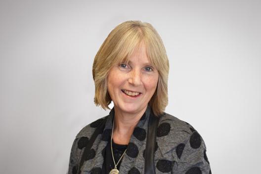 Frances smiling at the camera. She's a white woman with short blonde hair, wearing a grey and black jacket