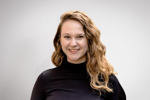 Rose smiling at the camera. She's a white woman with long wavy hair, wearing a black jumper