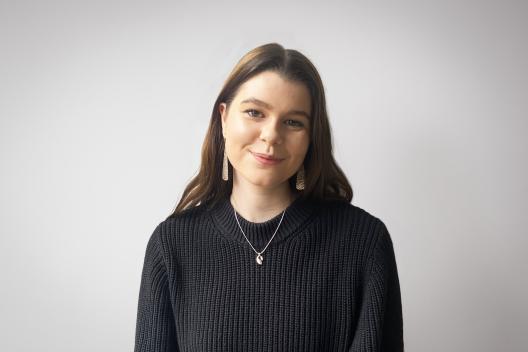Sophie smiling at the camera. She's a white woman with long brunette hair, wearing a black knitted jump and large silver earrings.