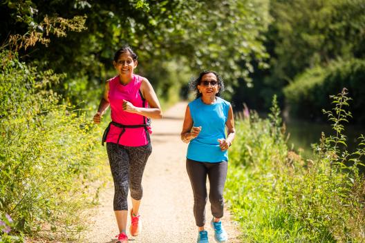 Two women in their 50s running along the canal in the sunshine