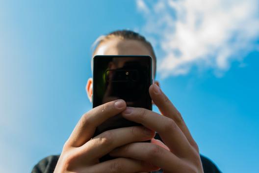 A teenage boy holds a smart phone up to the camera, blocking his face.
