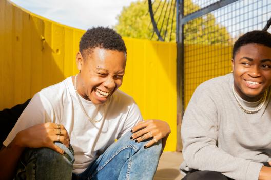 Two young people in front of a yellow background laughing