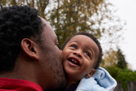 A black father kisses his baby son's cheek