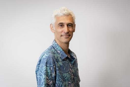 Aviv smiling at the camera. He's a man of colour with short grey hair, wearing a blue Hawaiian shirt