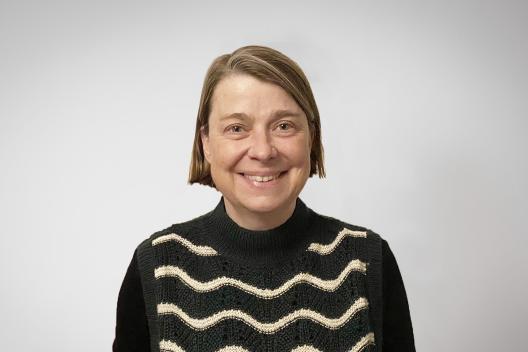 Charlotte smiling at the camera. She's a white woman with a brown bob, wearing a black and cream stripy jumper