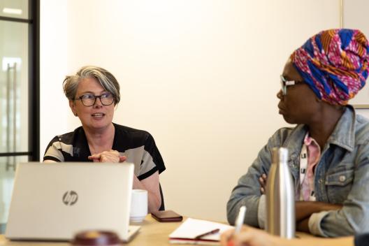Cath Dillon talking to a colleague with laptops and paper on the table
