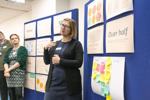 A woman talks in front of a board with posters