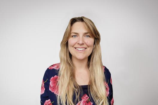Laura smiling at the camera. She's a white woman with long blonde hair, wearing a black and red flowery top
