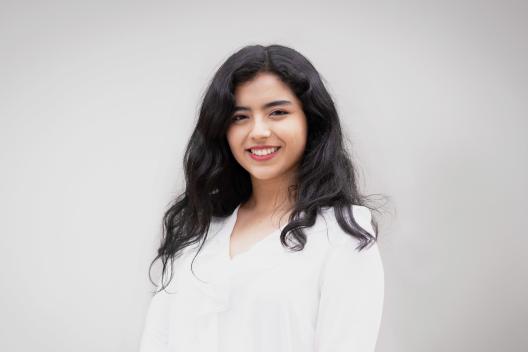 Liliana smiling at the camera. She's a woman of colour with long black hair, wearing a white shirt