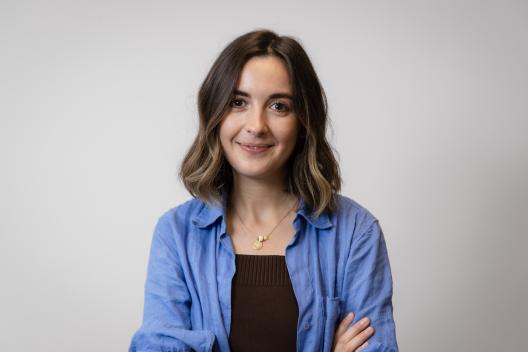 Sarah smiling at the camera. She's a white woman with shoulder-length brown hair, wearing a blue linen shirt