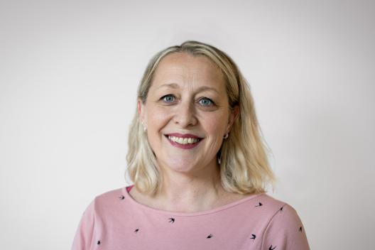 Lauren Jordan smiling at the camera. She has short blonde hair and is wearing a pink top.