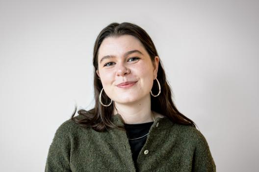 Sophie smiling at the camera. She's a white woman with long brunette hair, wearing a green knitted jumper