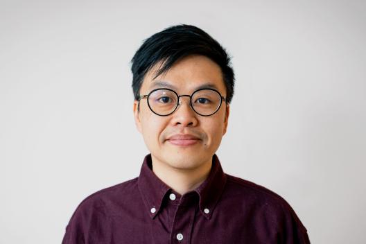 Yin Hei Ho looking at the camera. He is wearing glasses and a burgundy shirt.