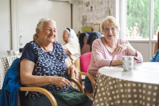 Two older women having tea at a busy community centre