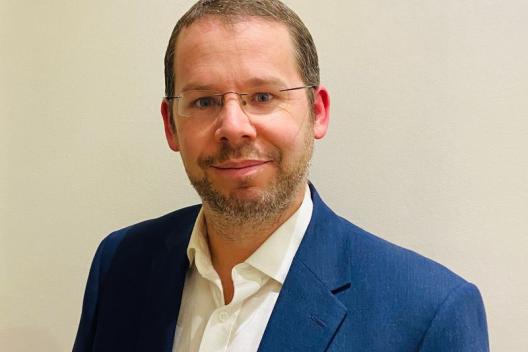 A man wearing glasses and a blue blazer and white shirt. 