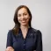 Lizzie is smiling at the camera. She is wearing a blue top, folding her arms and has brown hair. 