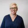 Heather smiling at the camera. She's a white woman with short blonde hair, wearing a black rimmed glasses