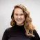 Rose smiling at the camera. She's a white woman with long wavy hair, wearing a black jumper