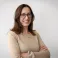Vicki smiling at the camera. She's a white woman with shoulder-length brown hair, wearing a beige jumper and black rimmed glasses