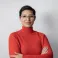 Jahaan smiling at the camera. She's a woman of colour with short brown hair, wearing a red turtleneck jumper and glasses