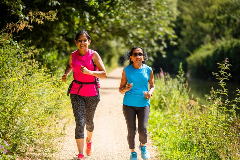 Two women in their 50s running along the canal in the sunshine