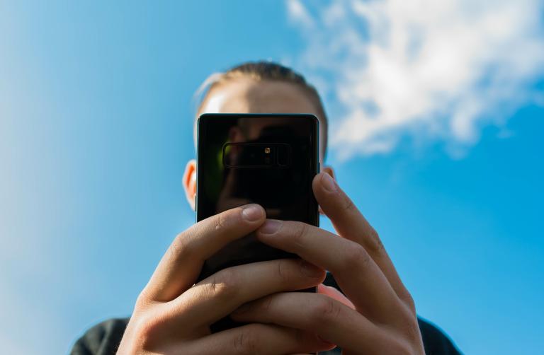 A teenage boy holds a smart phone up to the camera, blocking his face.