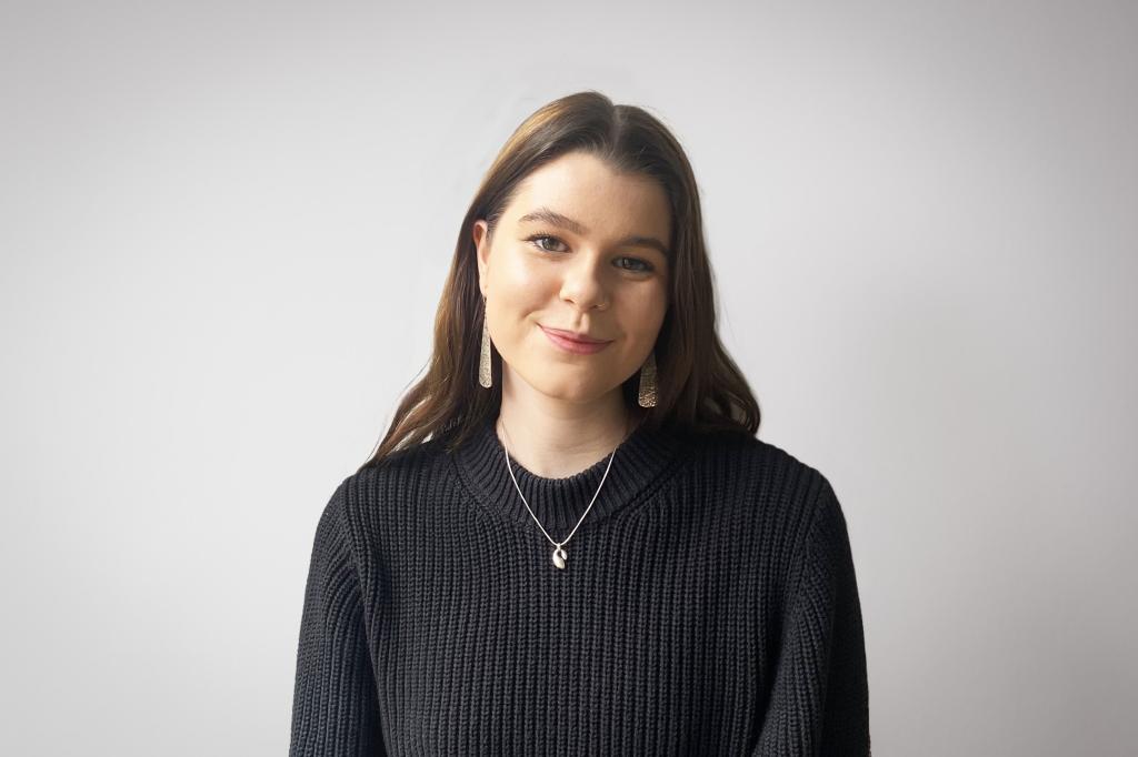 Sophie smiling at the camera. She's a white woman with long brunette hair, wearing a black knitted jump and large silver earrings.