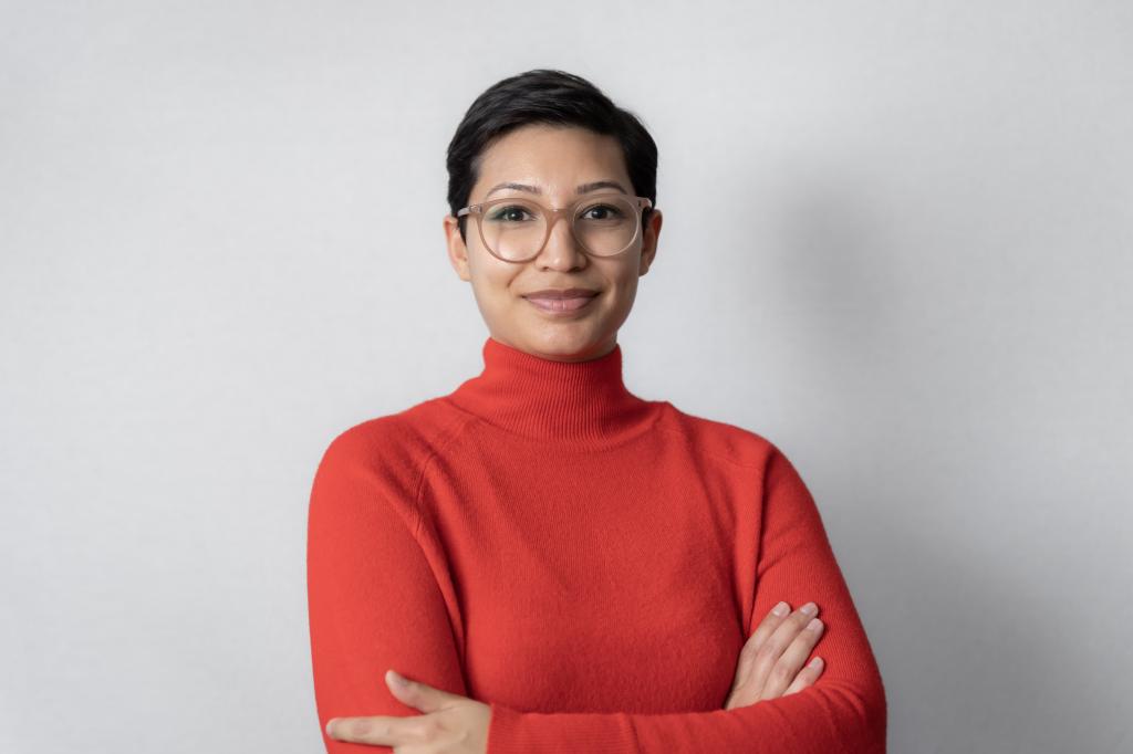 Jahaan smiling at the camera. She's a woman of colour with short brown hair, wearing a red turtleneck jumper and glasses