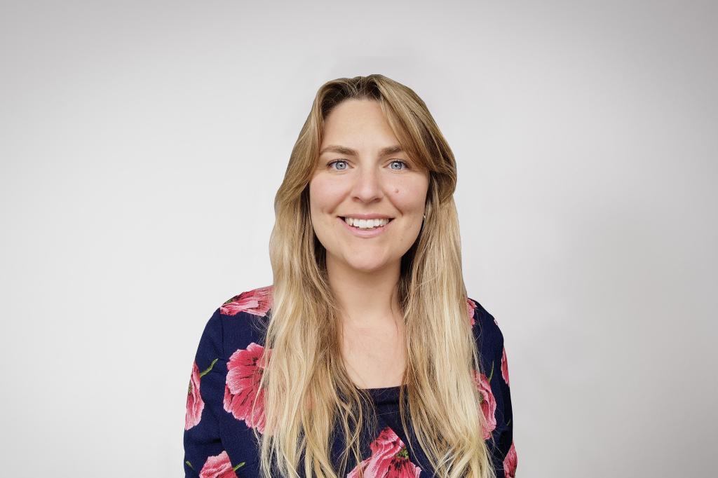Laura smiling at the camera. She's a white woman with long blonde hair, wearing a black and red flowery top