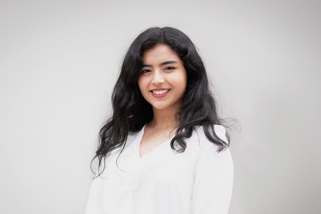 Liliana smiling at the camera. She's a woman of colour with long black hair, wearing a white shirt