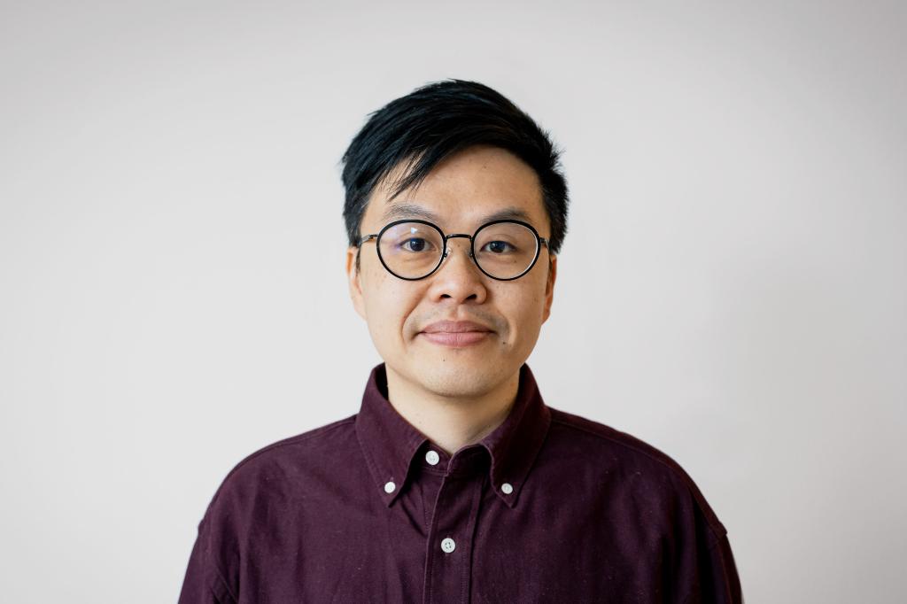 Yin Hei Ho looking at the camera. He is wearing glasses and a burgundy shirt.