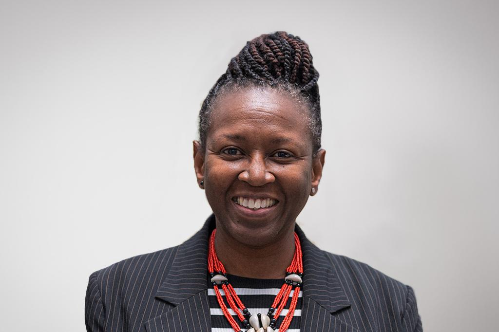 Sola smiling at the camera. She's a black woman with braided hair tied up. She is wearing a red necklace and a pinstriped jacket.