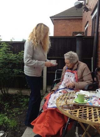 Elderly lady being given a cup of tea in the garden