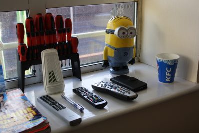 Window sill of personal possessions, including air freshener, remote controls, TV guide, cup, screwdrivers, phone and Minion figurine