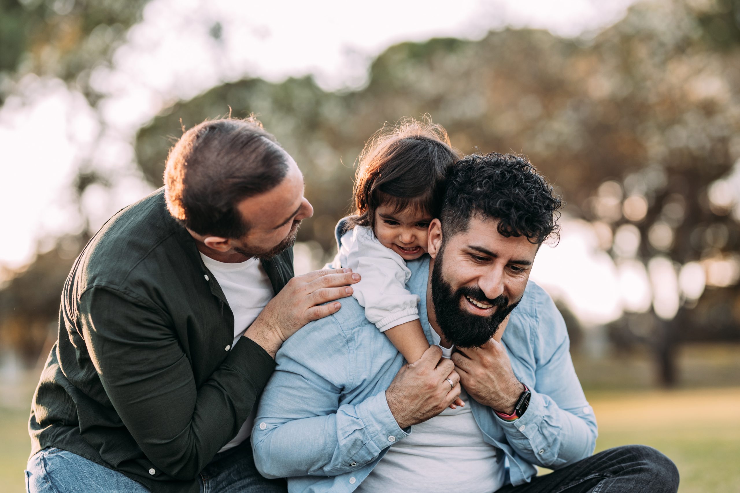 Gay parents enjoying with their girl in an urban park. Proud homosexual family concept.