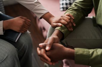 Young African American female psychologist keeping hand of wrist of male patient sitting in front of her and sharing his problems