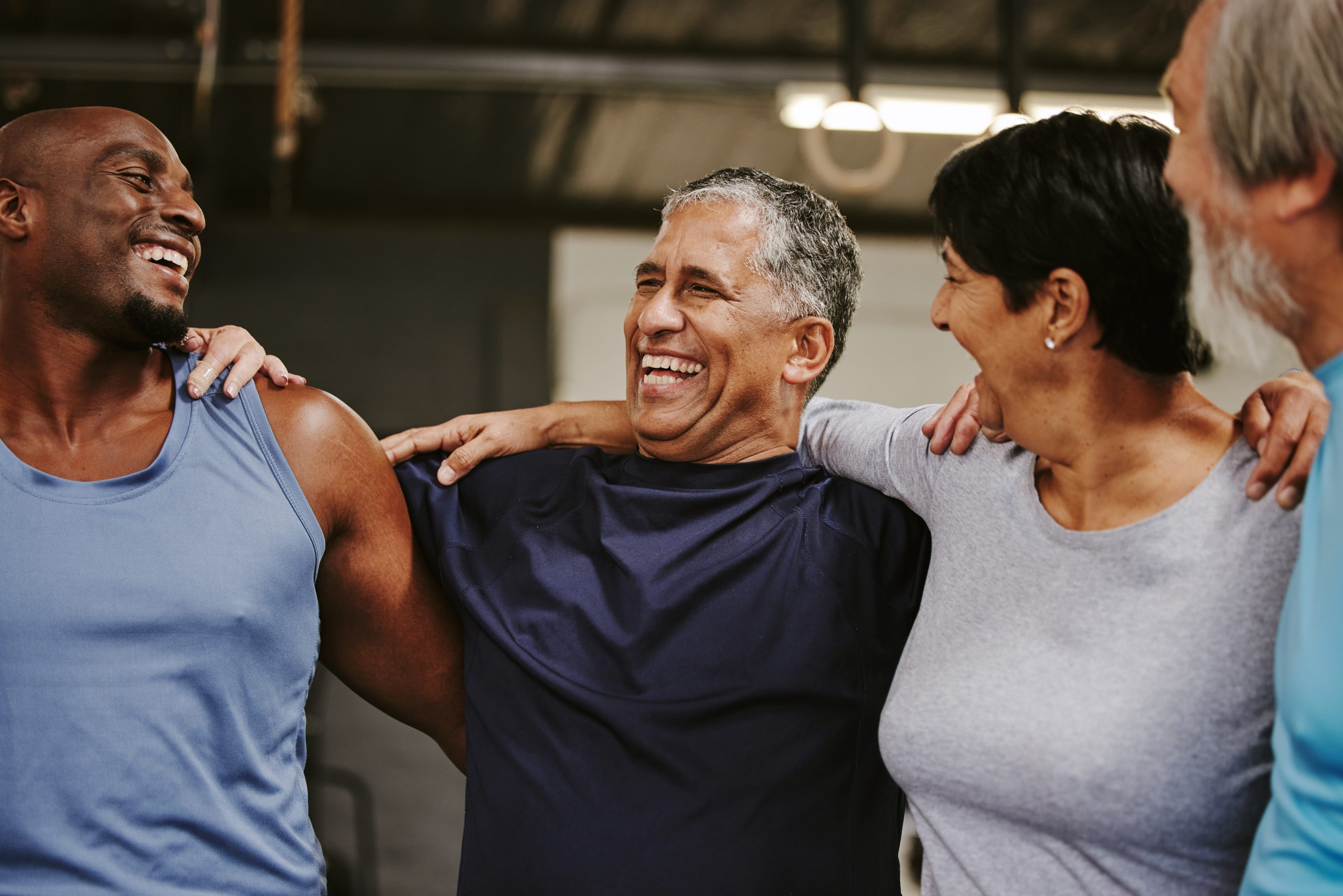 Senior people, fitness group and support for training, workout and exercise community or club in gym. Laugh, black people and elderly diversity friends with sports wellness hug together for teamwork.