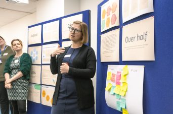 A woman speaking in front a large board covered in posters