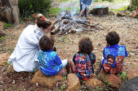 Woman sat with three children around a campfire